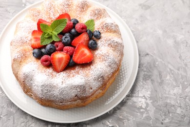 Photo of Tasty Bundt cake with powdered sugar and berries on grey textured table, closeup. Space for text