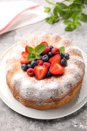 Photo of Tasty Bundt cake with powdered sugar and berries on grey textured table, closeup