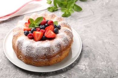Photo of Tasty Bundt cake with powdered sugar and berries on grey textured table, space for text