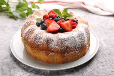 Photo of Tasty Bundt cake with powdered sugar and berries on grey textured table, closeup
