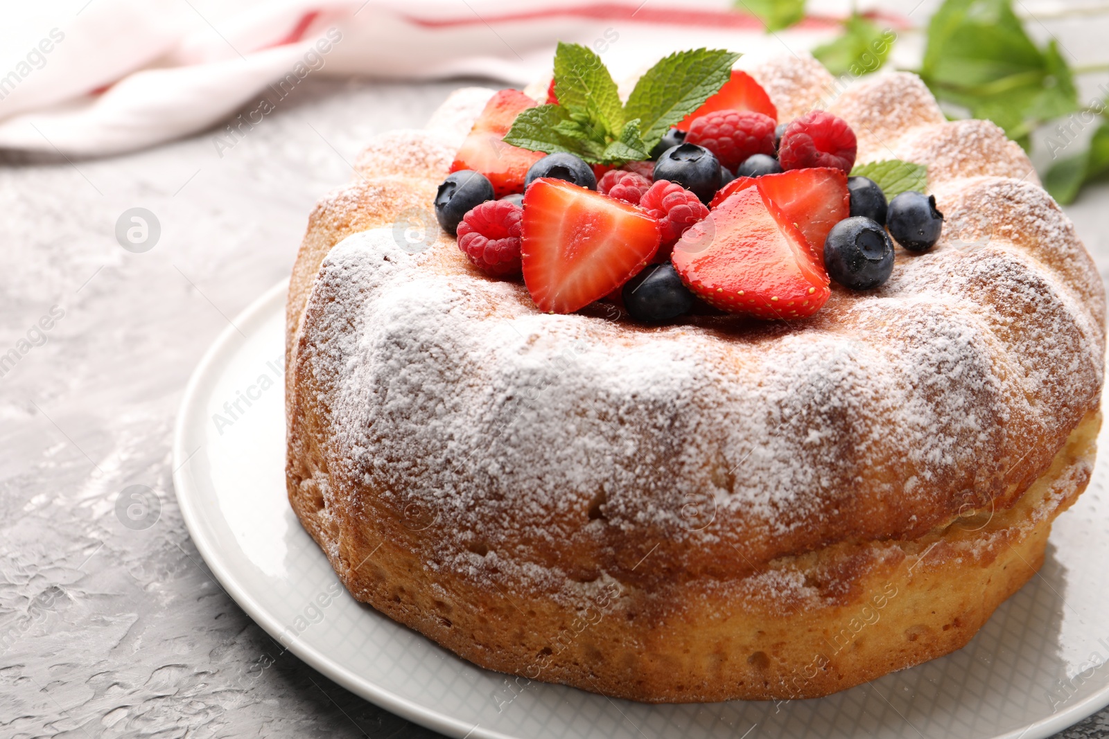 Photo of Tasty Bundt cake with powdered sugar and berries on grey textured table, closeup