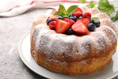 Photo of Tasty Bundt cake with powdered sugar and berries on grey textured table, closeup