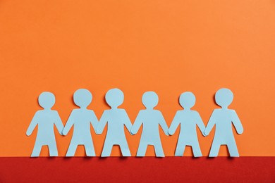 Photo of Human paper figures holding hands on color background, flat lay. Space for text