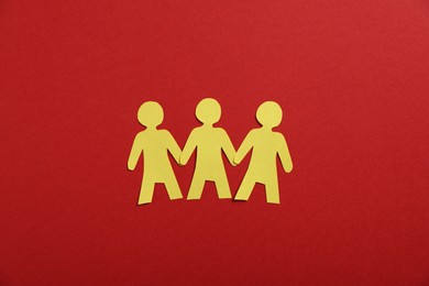 Photo of Human paper figures holding hands on red background, flat lay