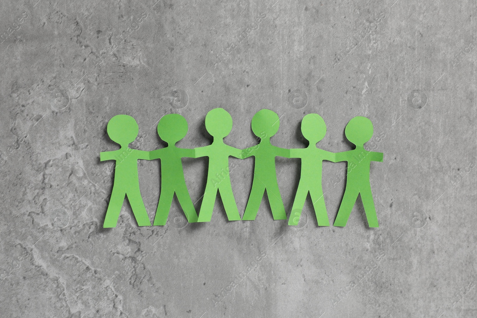 Human paper figures holding hands on grey background, flat lay Photo of Human paper figures holding hands on grey background, flat lay