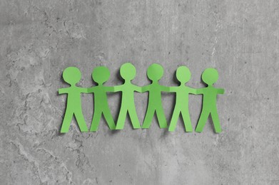 Photo of Human paper figures holding hands on grey background, flat lay