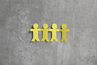 Photo of Human paper figures holding hands on grey background, flat lay