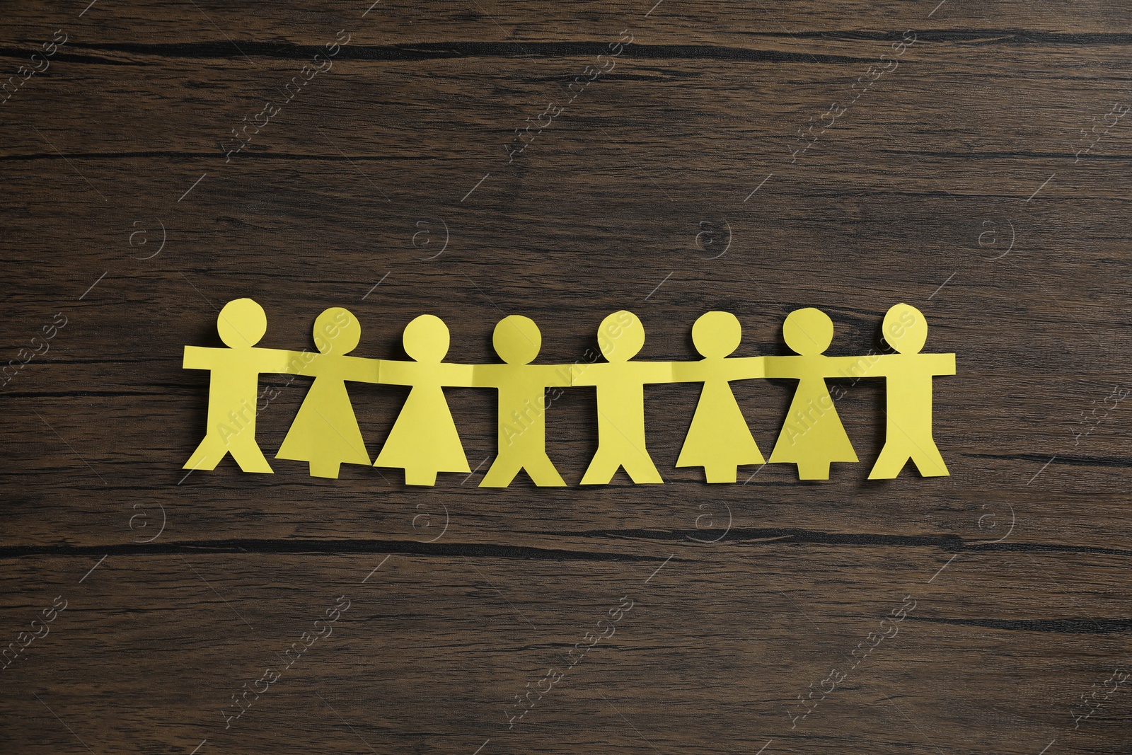 Photo of Human paper figures holding hands on wooden background, flat lay