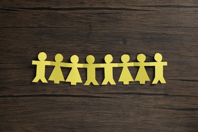 Photo of Human paper figures holding hands on wooden background, flat lay