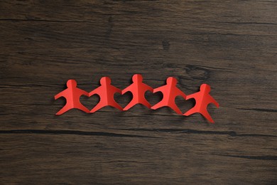 Photo of Human paper figures holding hands on wooden background, flat lay