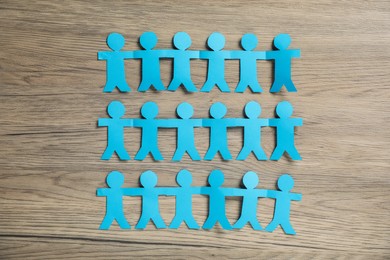 Photo of Human paper figures holding hands on wooden background, flat lay