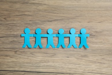 Photo of Human paper figures holding hands on wooden background, flat lay