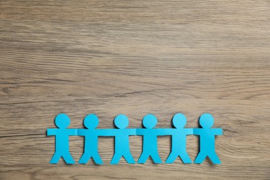 Photo of Human paper figures holding hands on wooden background, flat lay