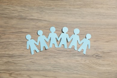 Photo of Human paper figures holding hands on wooden background, flat lay