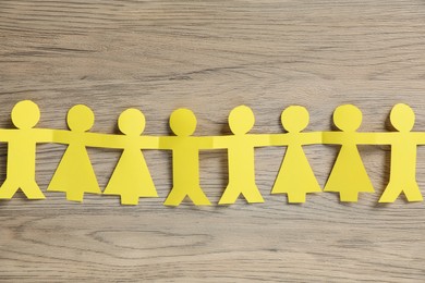 Photo of Human paper figures holding hands on wooden background, flat lay
