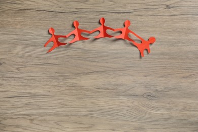 Photo of Human paper figures holding hands on wooden background, flat lay. Space for text