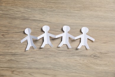 Photo of Human paper figures holding hands on wooden background, flat lay