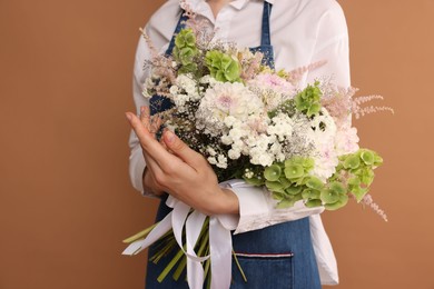 Photo of Florist with beautiful bouquet of flowers on dark beige background, closeup
