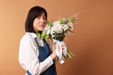 Photo of Florist with beautiful bouquet of flowers on dark beige background, space for text