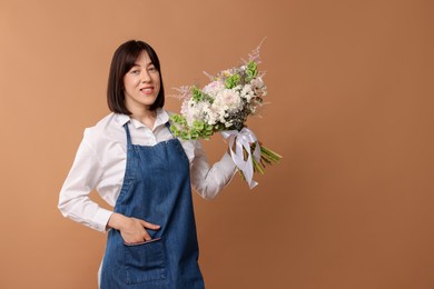 Photo of Florist with beautiful bouquet of flowers on dark beige background, space for text