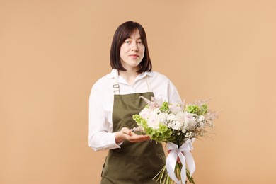 Photo of Florist with beautiful bouquet of flowers on beige background