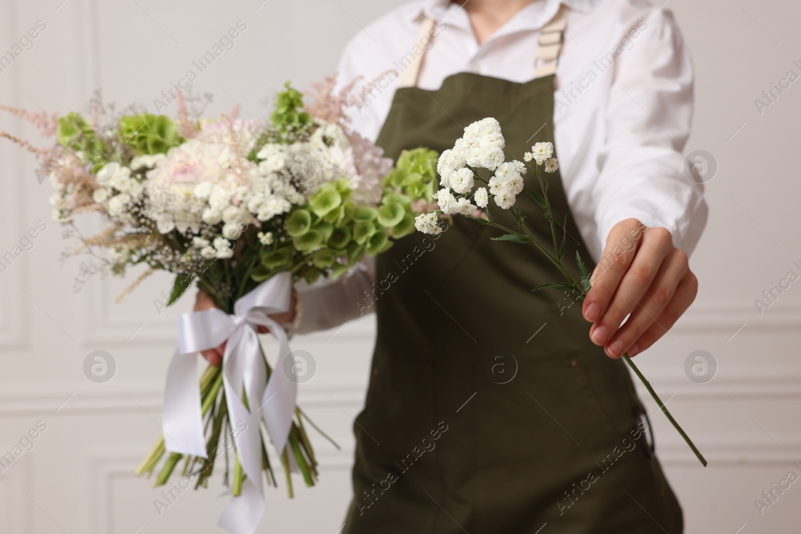Florist with beautiful bouquet of flowers near white wall indoors, closeup Photo of Florist with beautiful bouquet of flowers near white wall indoors, closeup