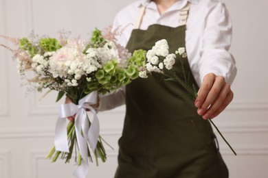 Photo of Florist with beautiful bouquet of flowers near white wall indoors, closeup