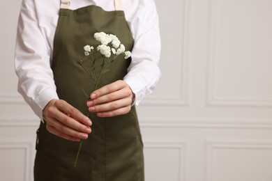 Photo of Florist with beautiful flowers near white wall indoors, closeup. Space for text