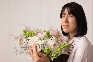 Photo of Florist with beautiful bouquet of flowers near white wall indoors