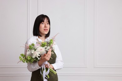 Photo of Florist with beautiful bouquet of flowers near white wall indoors, space for text
