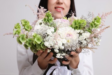 Photo of Florist with beautiful bouquet of flowers near white wall indoors, closeup