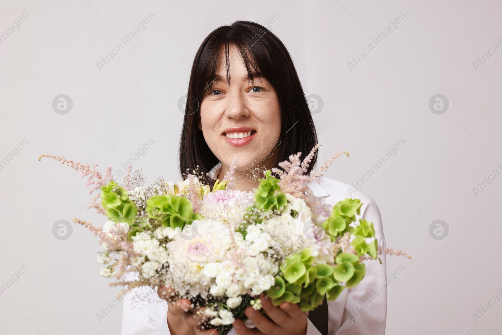 Florist with beautiful bouquet of flowers near white wall indoors Photo of Florist with beautiful bouquet of flowers near white wall indoors