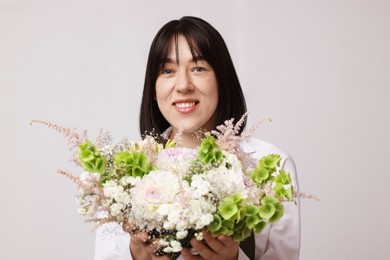 Photo of Florist with beautiful bouquet of flowers near white wall indoors