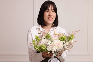 Photo of Florist with beautiful bouquet of flowers near white wall indoors