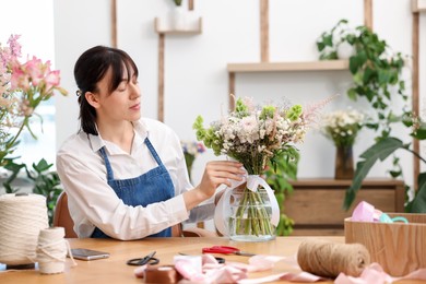 Photo of Florist making bouquet of flowers at wooden table indoors