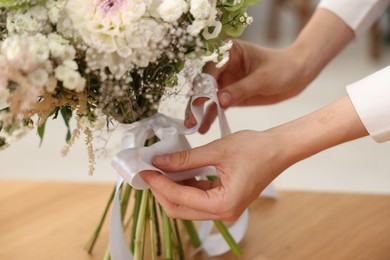 Photo of Florist making bouquet of flowers at table indoors, closeup