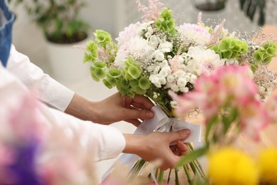 Photo of Florist making bouquet of flowers at table indoors, closeup