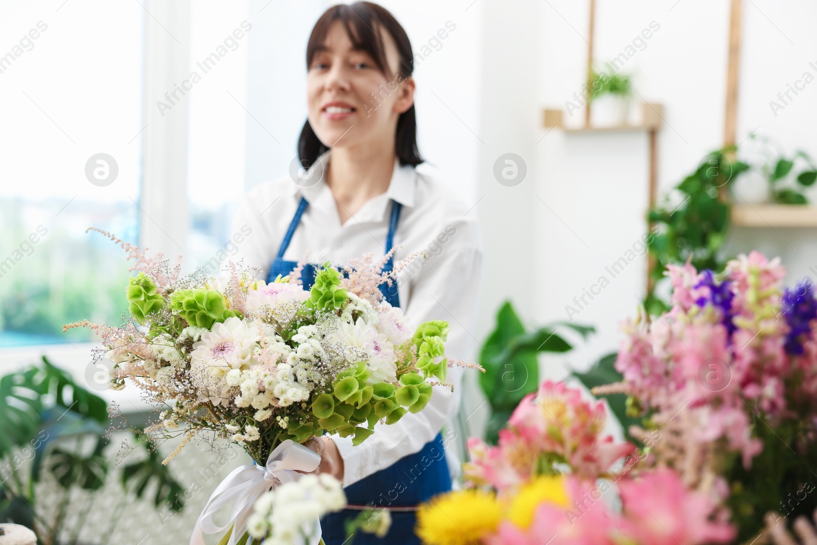 Photo of Florist with beautiful bouquet of flowers indoors, selective focus