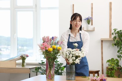 Photo of Florist with beautiful bouquet of flowers at table indoors