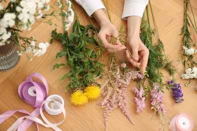 Photo of Florist making bouquet of flowers at wooden table, top view