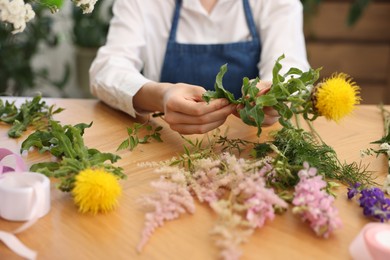 Photo of Florist making bouquet of flowers at wooden table indoors, closeup