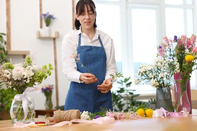 Photo of Florist making bouquet of flowers at table indoors