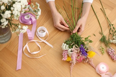 Photo of Florist making bouquet of flowers at wooden table, top view