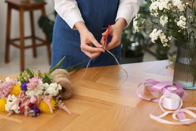 Photo of Florist making bouquet of flowers at wooden table indoors, closeup