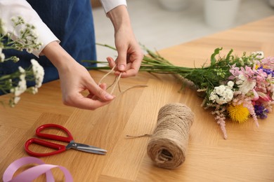 Photo of Florist making bouquet of flowers at wooden table indoors, closeup