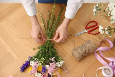Photo of Florist making bouquet of flowers at wooden table, top view