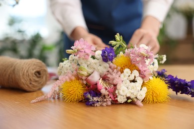 Photo of Florist making bouquet of flowers at wooden table indoors, closeup