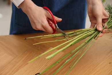 Photo of Florist making bouquet of flowers at wooden table indoors, closeup