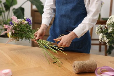 Photo of Florist making bouquet of flowers at wooden table indoors, closeup