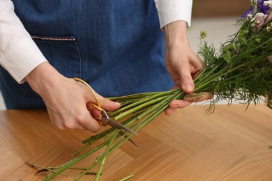Photo of Florist making bouquet of flowers at wooden table indoors, closeup